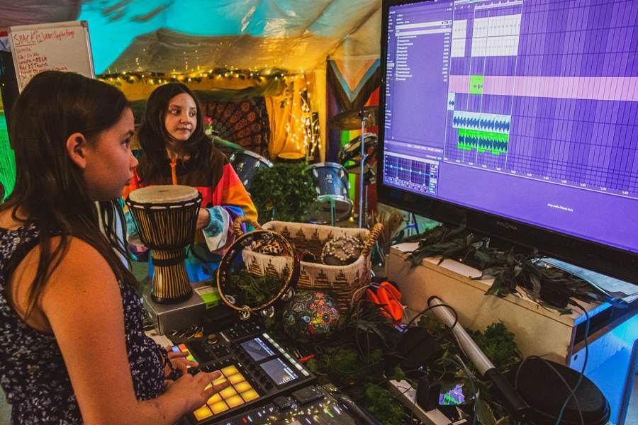 Two campers building a beat on a drum pad in front of a big Ableton screen