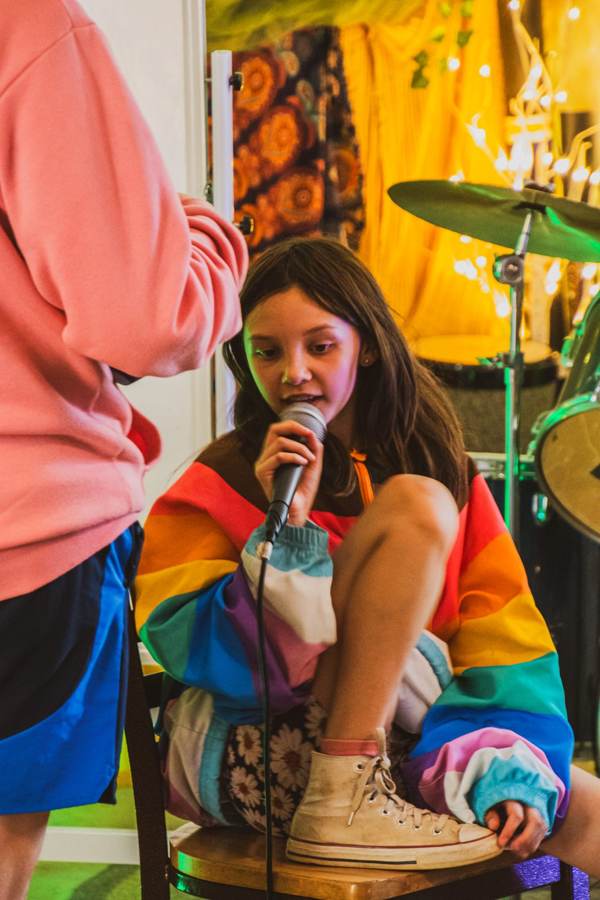 A camper in a rainbow jacket sings into a mic in the studio tent